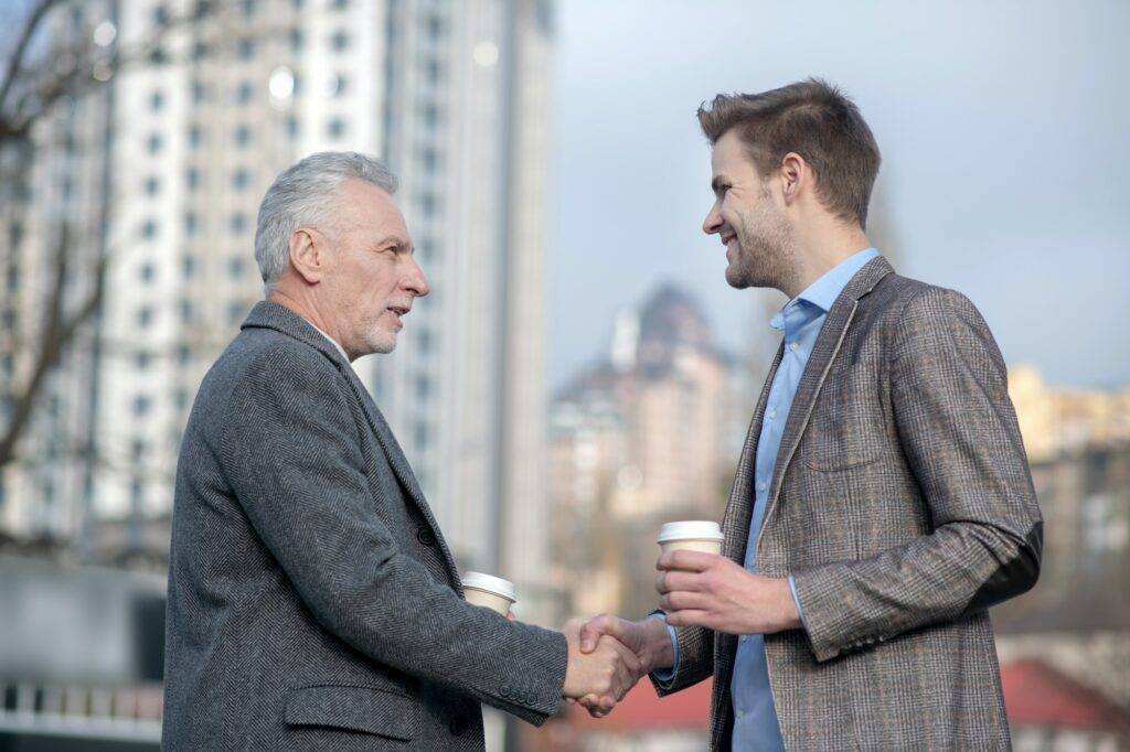 Young businessman and his mature mentor shaking hands